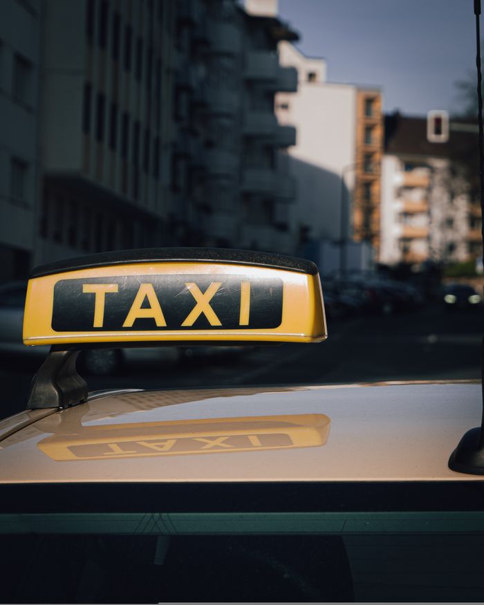 gallery-2 Close-up of a taxi sign on a car roof with an urban city background.