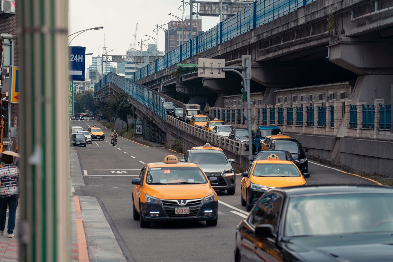 services-04 Yellow taxis and vehicles navigating an urban street under an overpass.
