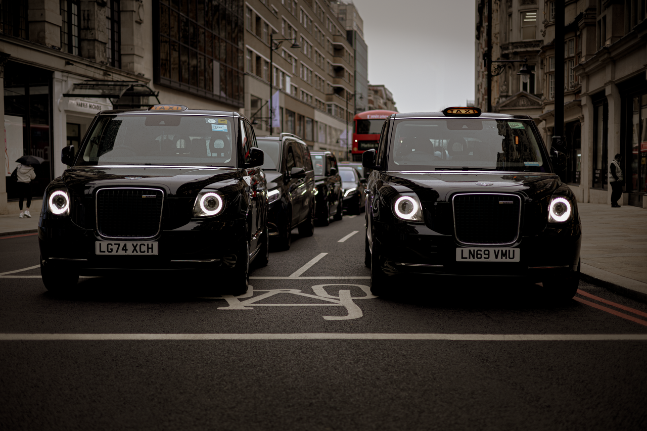 why-choose-us Black taxis line up on a London street showcasing modern urban transportation.