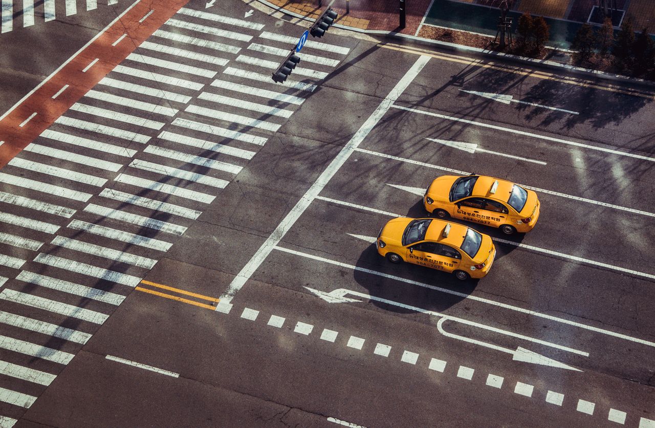 services-02 Two yellow taxis navigate a city intersection with marked pedestrian crossings.