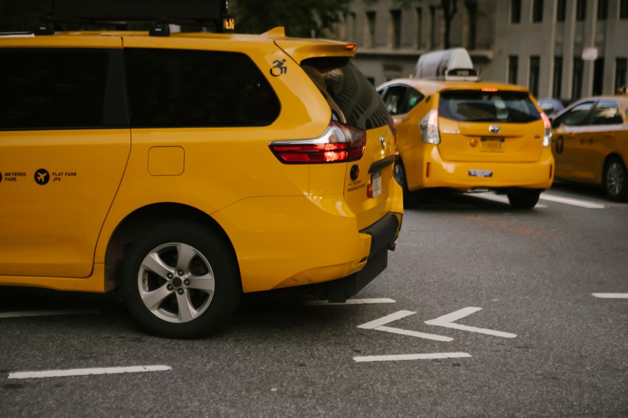 gallery-1 Modern yellow crossover taxi cars riding on asphalt road near commercial buildings in city