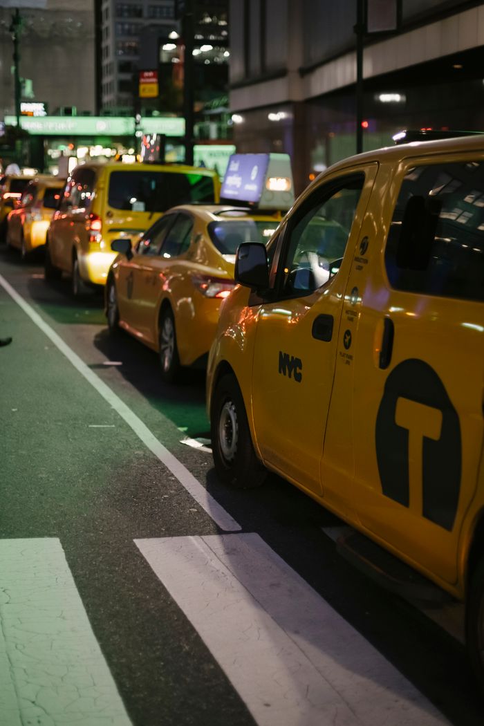 services-01 Row of modern various yellow taxi vehicles parked on city street near buildings in New York at night